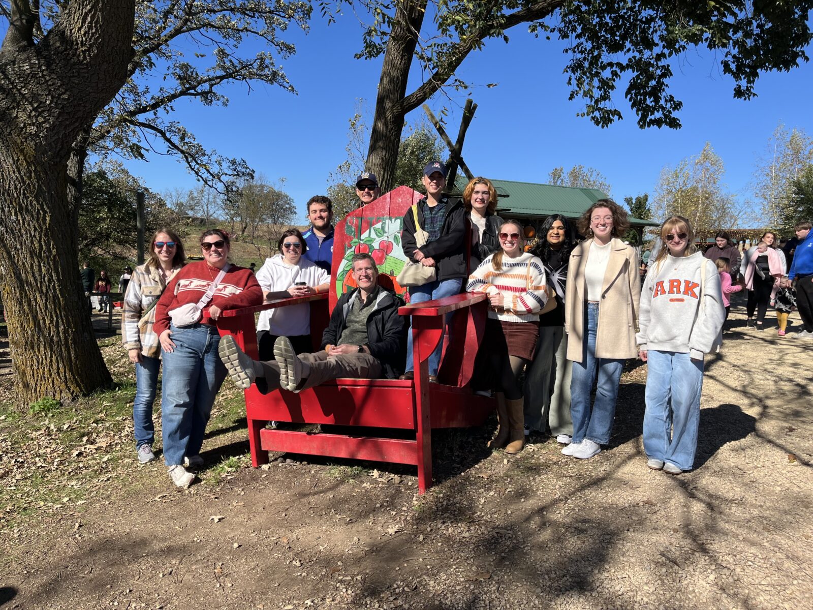 Group of people standing around an oversized chair smiling